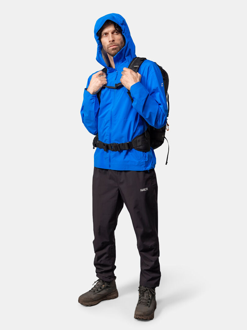 Man wearing Halti Pisarat 2,5L DX Shell Jacket Men's, black pants, hiking boots, and a black backpack.