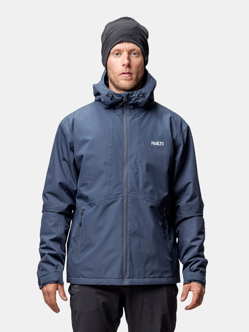 A man wears a Halti Forter DX Warm Shell Jacket in dark blue with a hood and a black beanie, against a plain background.
