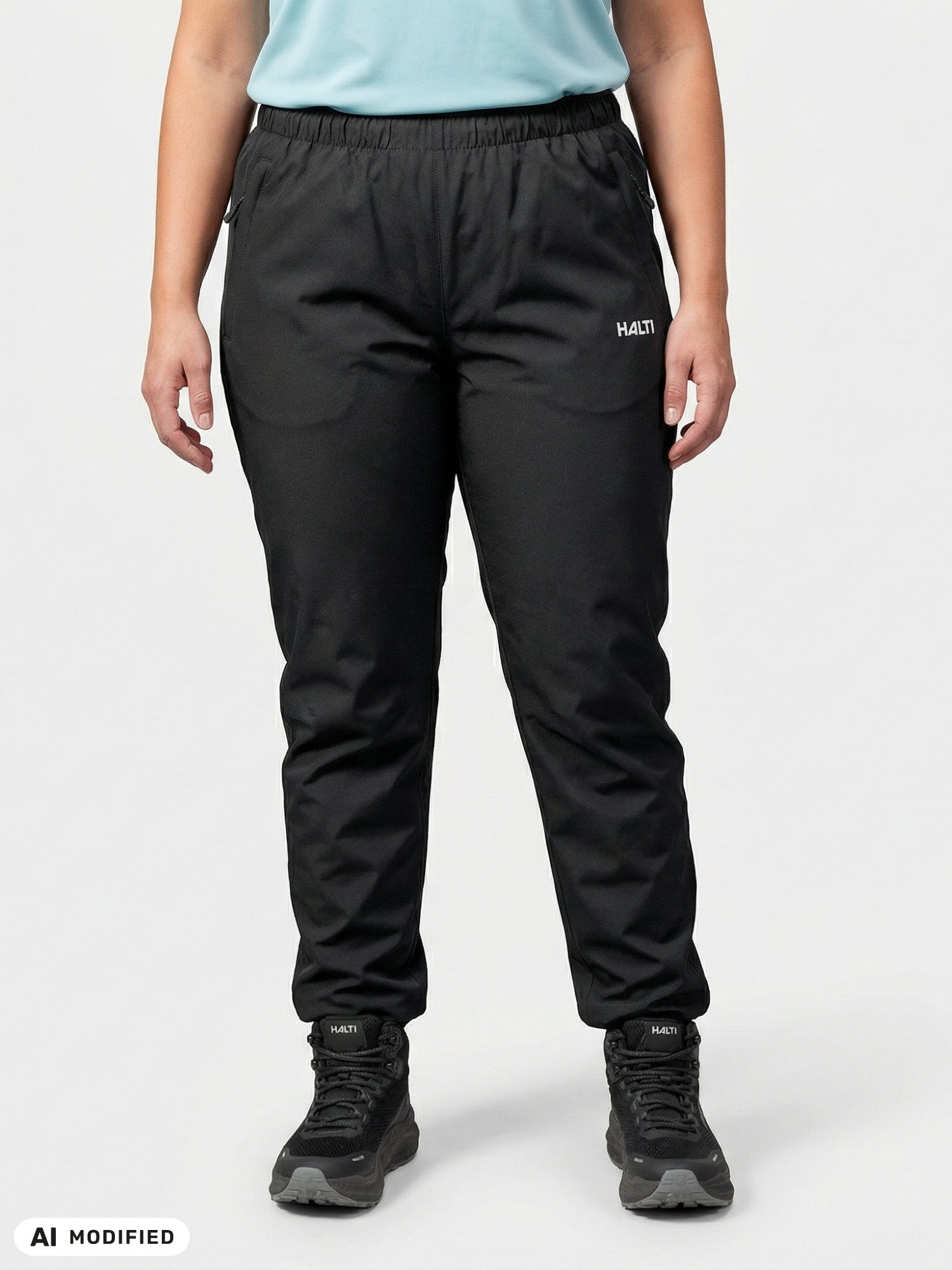 Model wears Halti Forter DX Shell Pants Women's Plus in black with sneakers, standing against a light background.