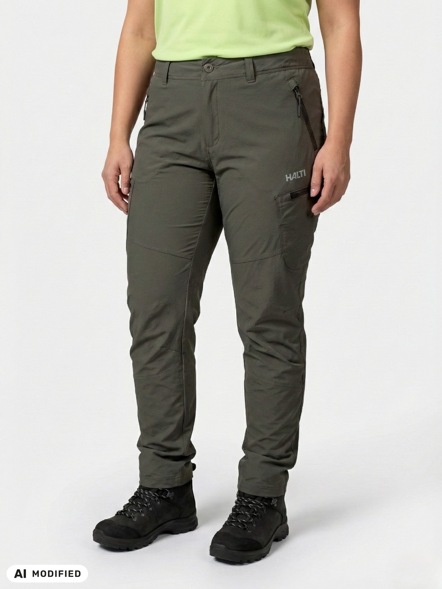 A person in Halti Pallas Evo Plus X-stretch pants, black boots, and a light green shirt stands against a plain background.