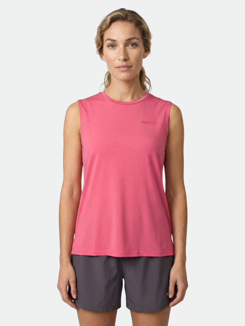 A woman wears the Halti Kalteva Top Women's, a sleeveless pink trekking top, with dark shorts against a plain background.