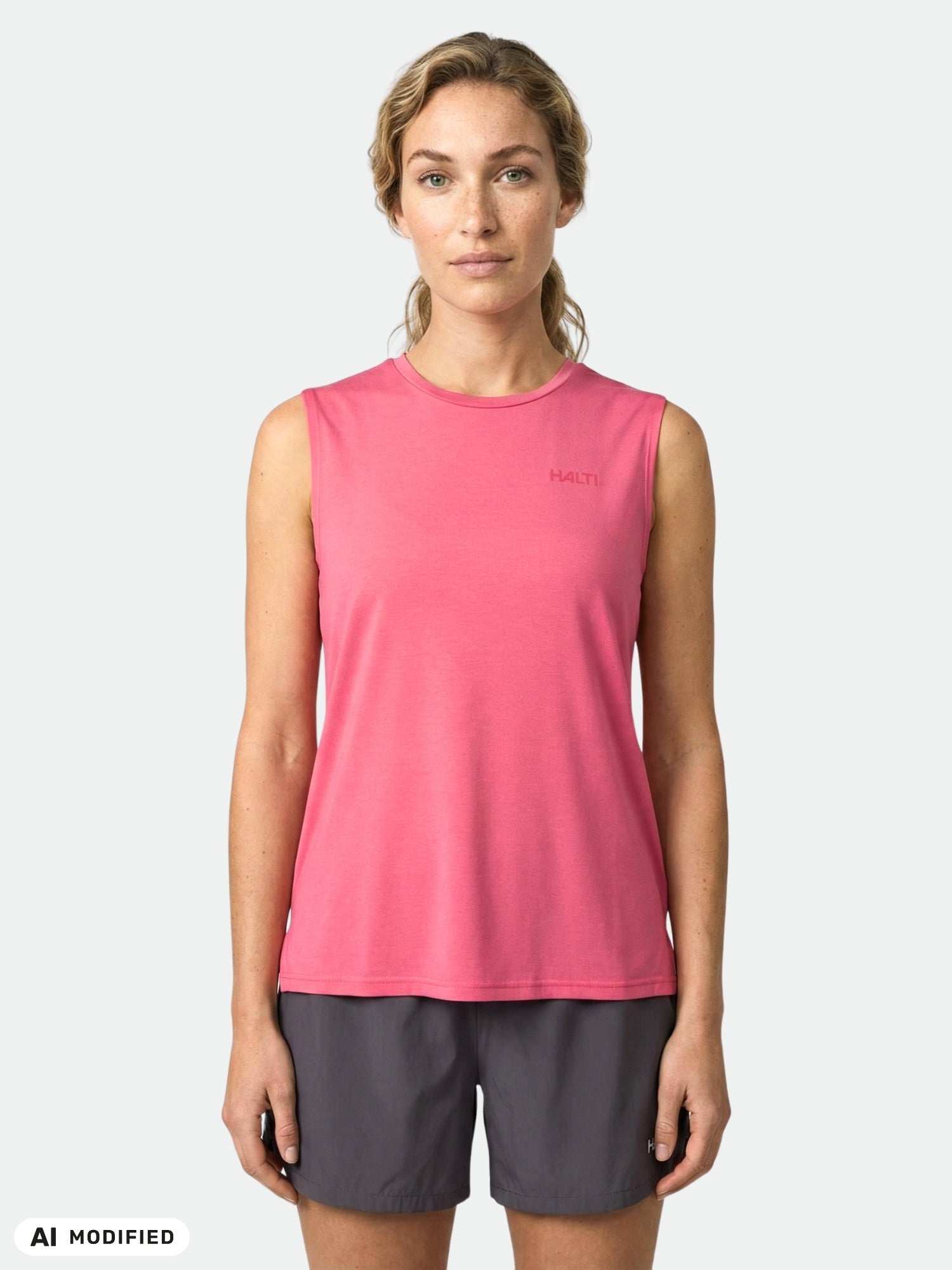 A woman faces forward in a sleeveless pink Halti Kalteva Top Women's and dark shorts against a plain background.