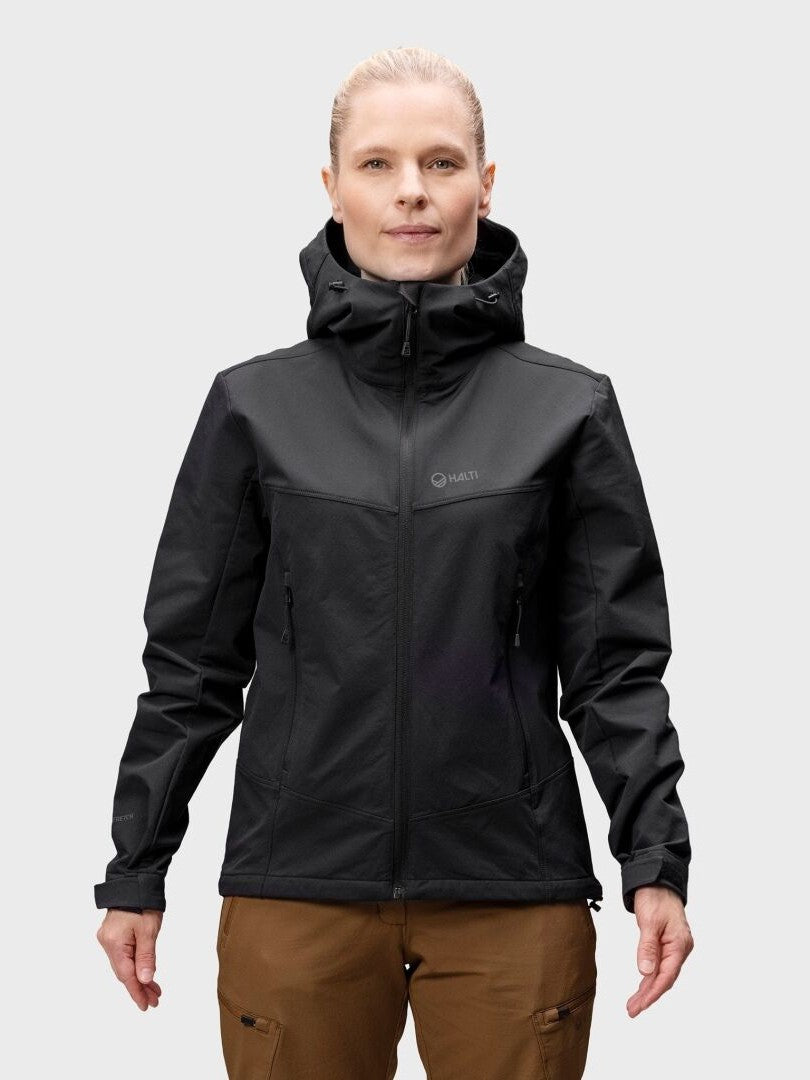 A woman wears the Halti Pallas Evo Brushed X-stretch Jacket, black, paired with brown pants against a light gray background.