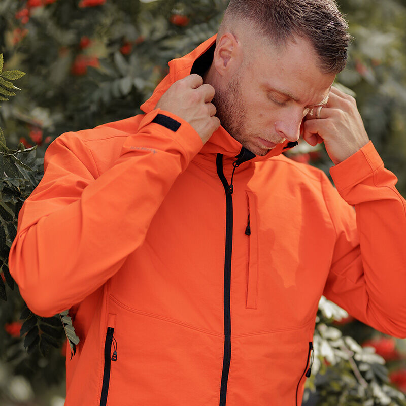 A man in a Halti Pallas Evo Brushed X-stretch Jacket adjusts the hood near leafy branches with red berries.