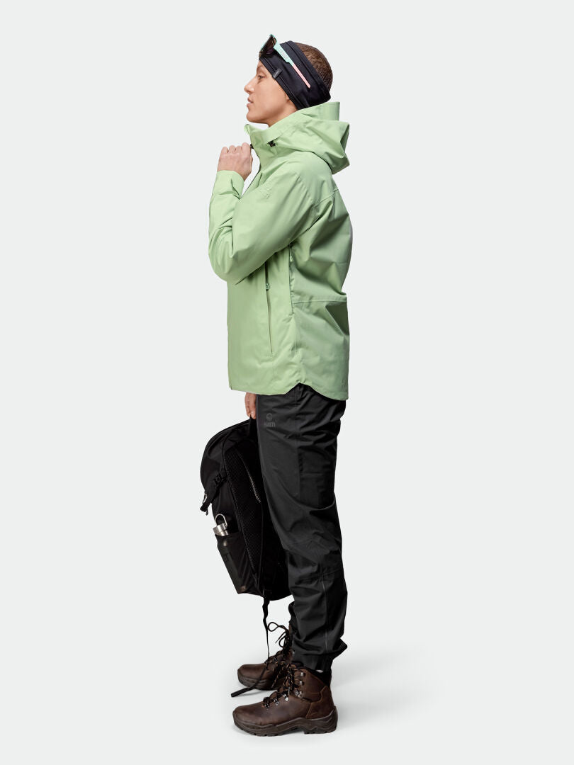 Woman in Halti Staala DrymaxX Shell Jacket stands in profile with black pants, boots, black bag, and headband.