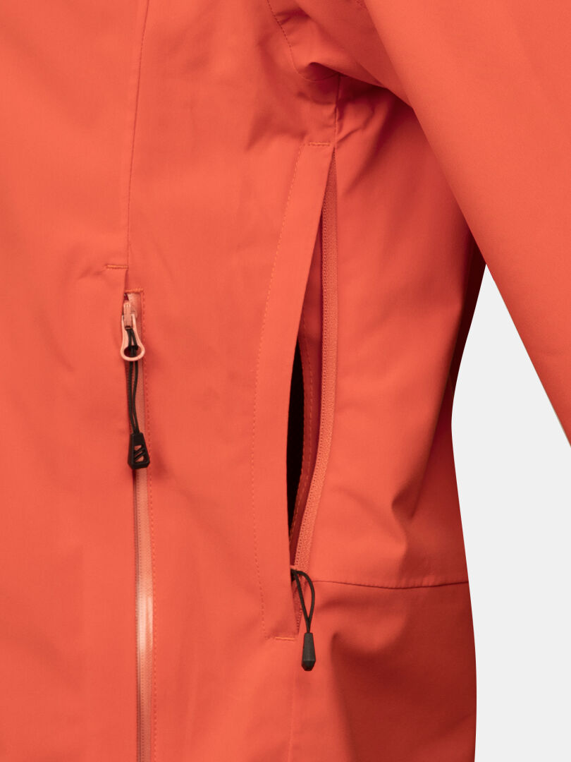 Close-up of the Halti Staala DX Shell Jacket Women's in orange, featuring a front zipper and partially open side pocket.
