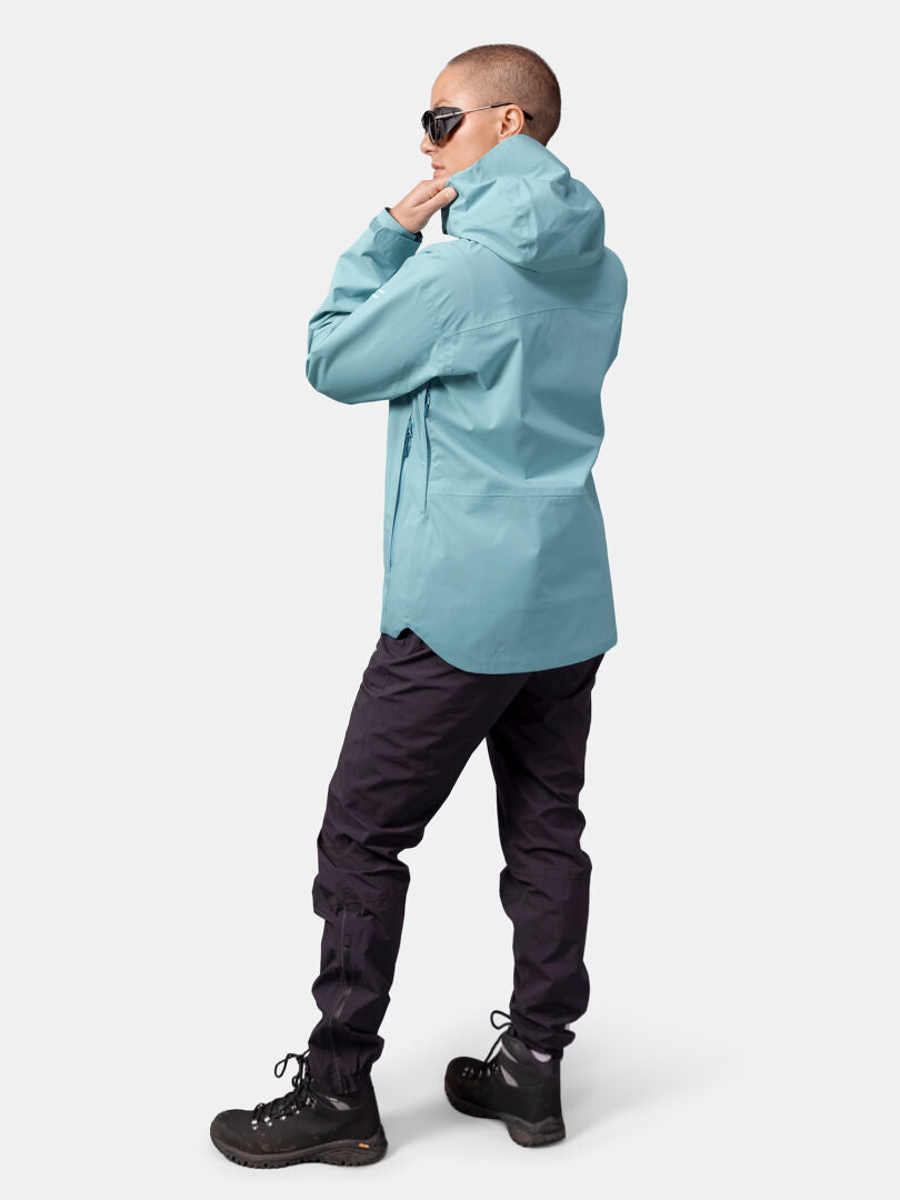 Woman in Halti Staala DX Shell Jacket, black pants, boots, and sunglasses stands looking to the side.