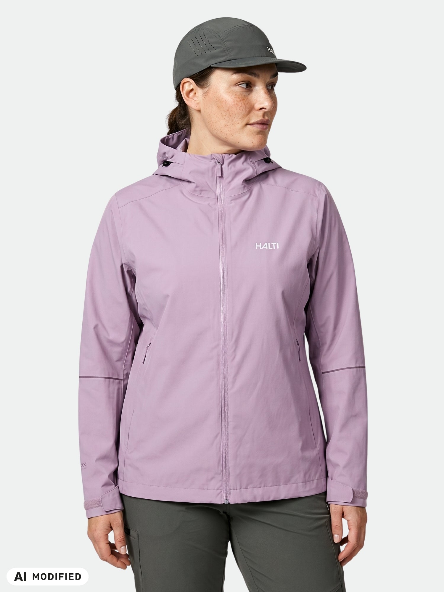 Person wearing a light purple Halti Staala DX Shell Jacket Women's Plus, gray cap, and dark pants against a white background.
