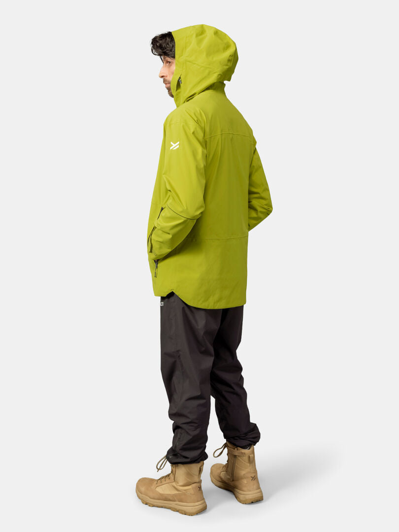 A man wears the Halti Staala DX Shell Jacket, black pants, and tan boots, standing sideways against a plain background.