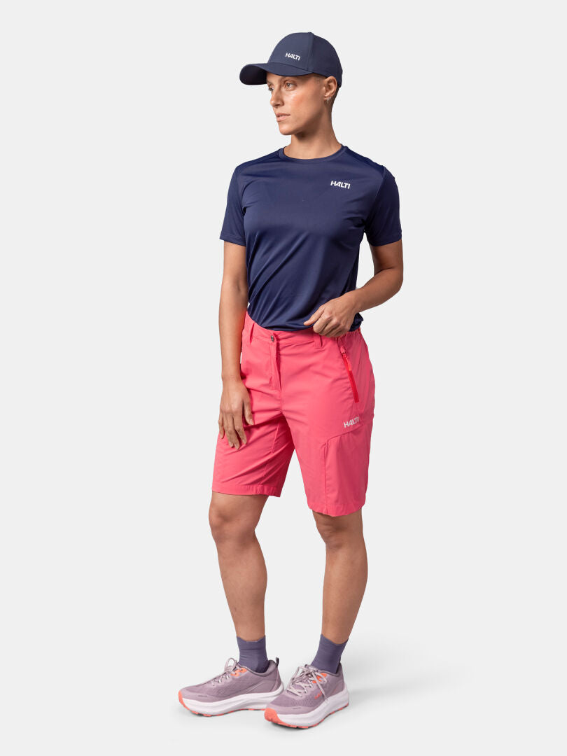 Person in a navy cap, navy t-shirt, and Halti Pallas Cool Shorts Women's stands against a plain light background.