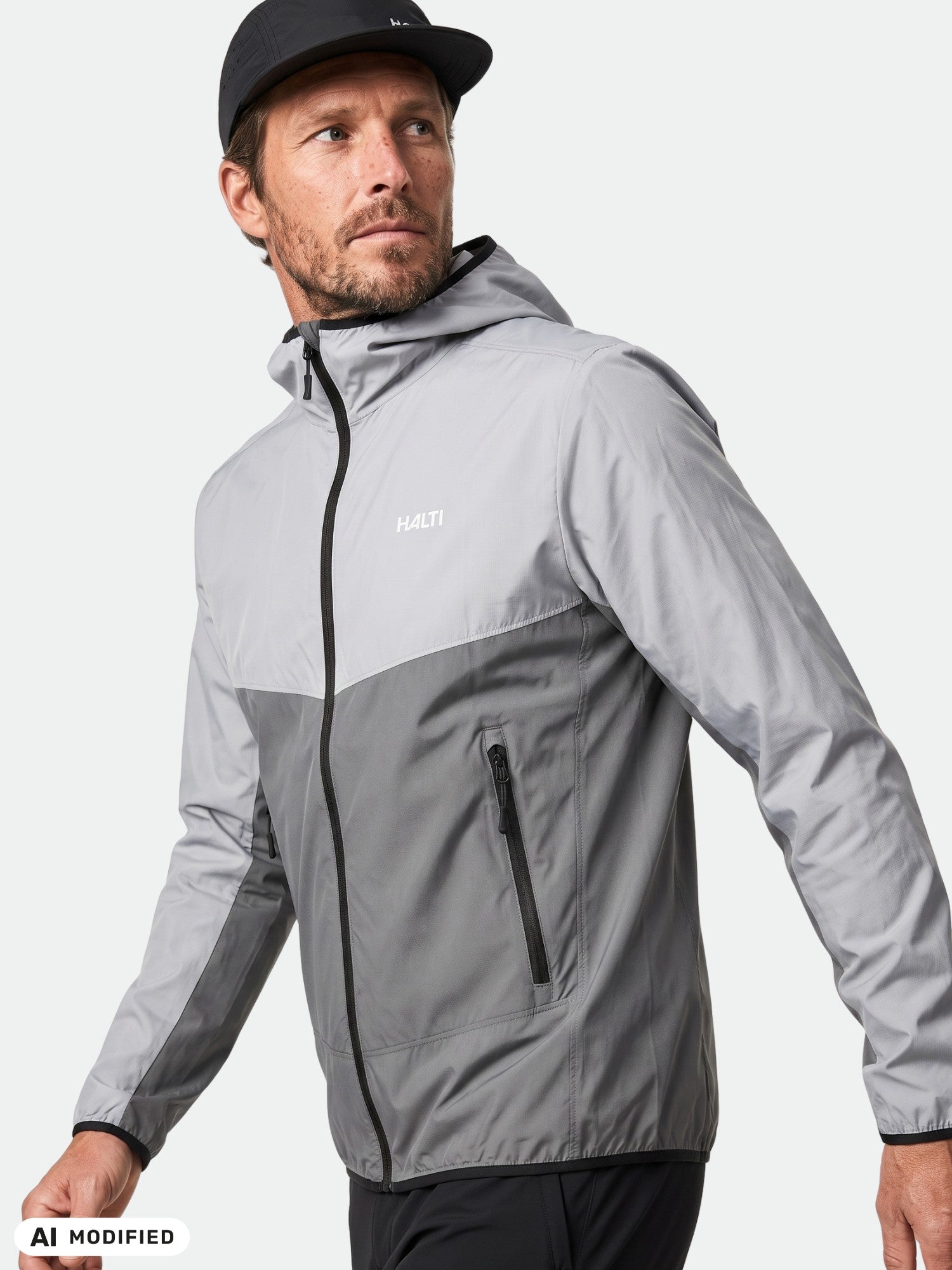 Man in Halti Pallas Cool X-stretch Jacket with hood and black zipper, wearing black cap, walking forward.