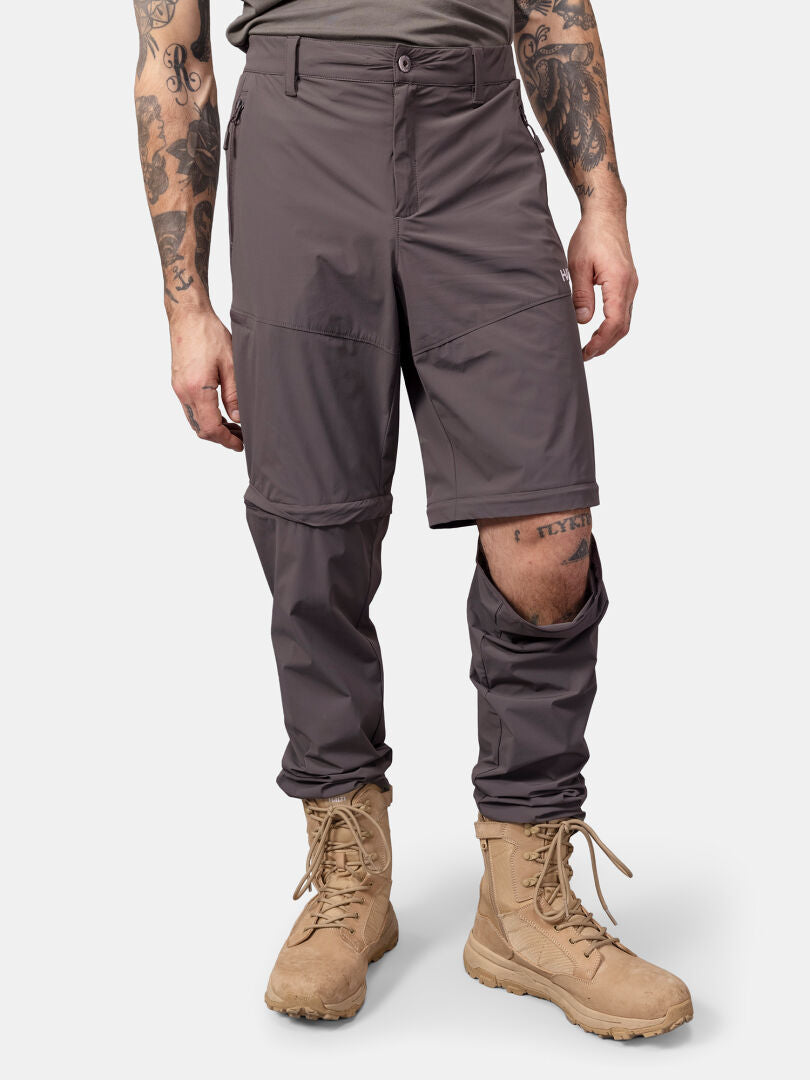 Man wearing Halti Pallas Cool Stretch Zip-off Pants with one leg unzipped, tan boots, and tattoos on arms and leg.