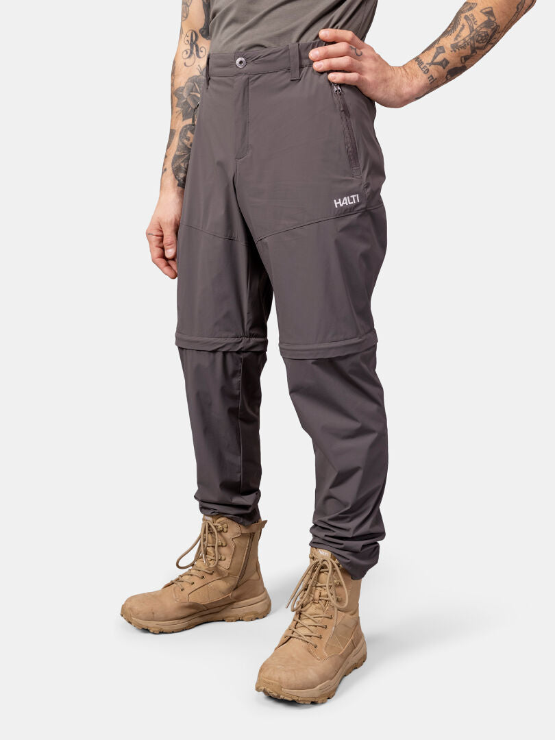 Man wearing Halti Pallas Cool Stretch Zip-off Pants, tan boots, and a gray shirt against a white background.
