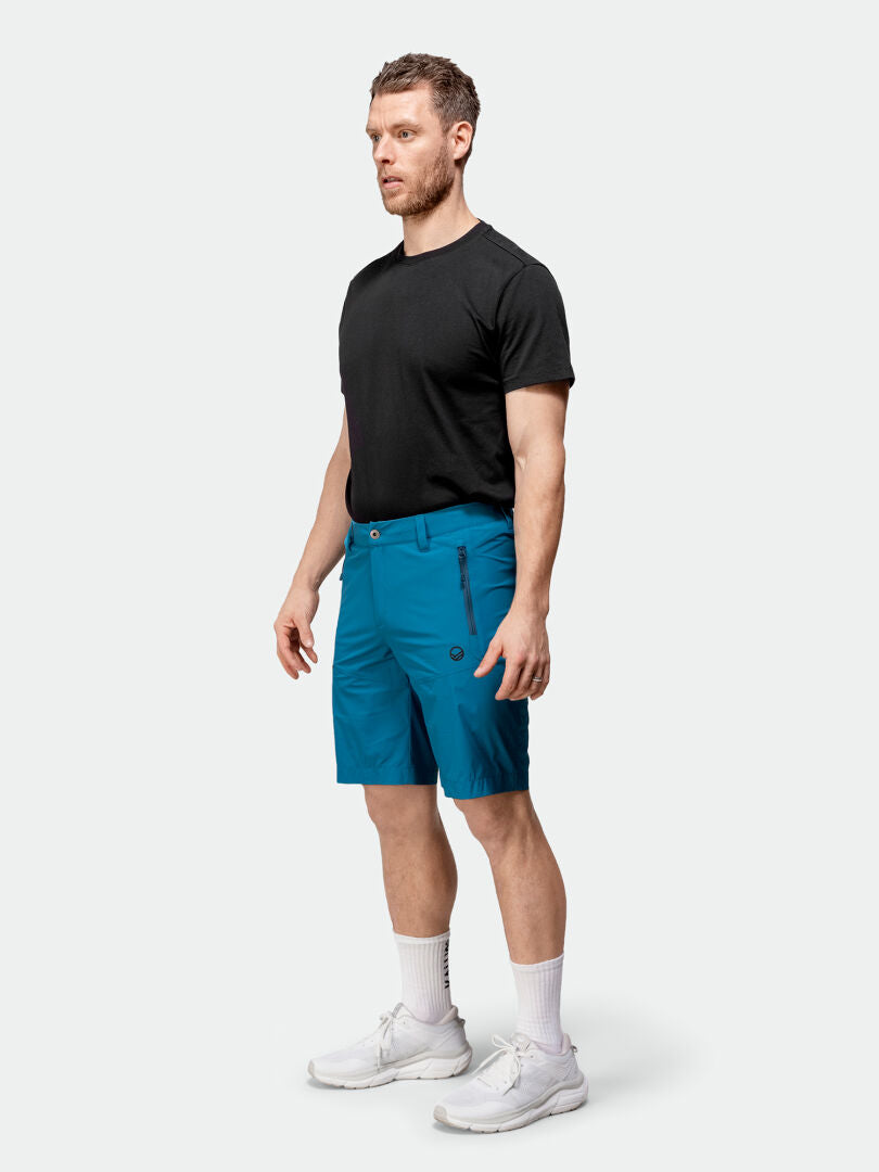 A man faces left, wearing Halti Pallas Cool X-stretch Shorts, a black t-shirt, white socks, and sneakers.
