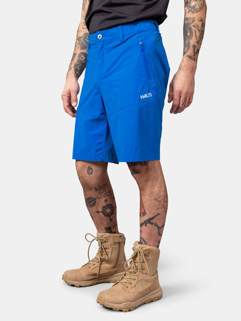 Person wearing Halti Pallas Cool X-stretch Shorts in bright blue, tan boots, black shirt, and visible tattoos.