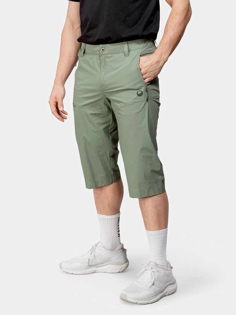 A person in Halti Pallas Cool X-stretch Capri Pants, a black shirt, white socks, and sneakers stands hands in pockets.