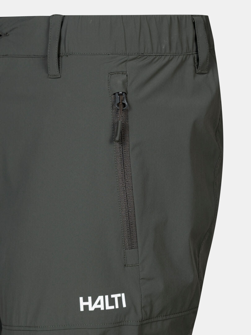 Close-up of Halti Pallas Cool X-stretch men's capri pants in dark gray with vertical zip pocket and logo near the hem.