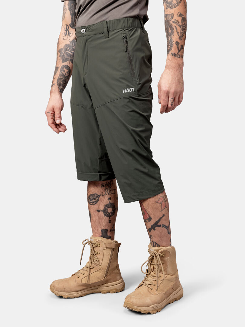 A man in Halti Pallas Cool X-stretch Capri Pants, tan boots, grey shirt, and with tattooed arms and legs.