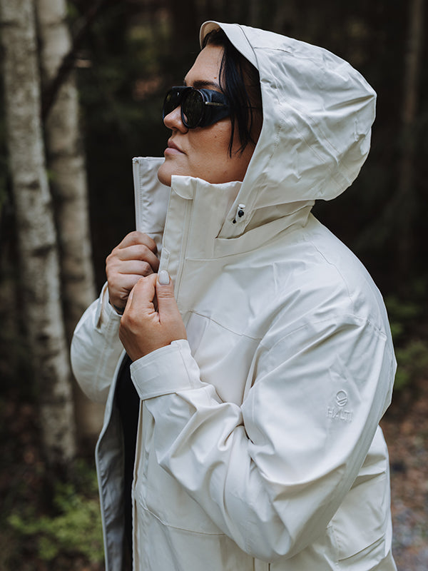 A person in a Halti Kallas DX Parka Jacket Plus Womens and black sunglasses stands outdoors in a wooded area.