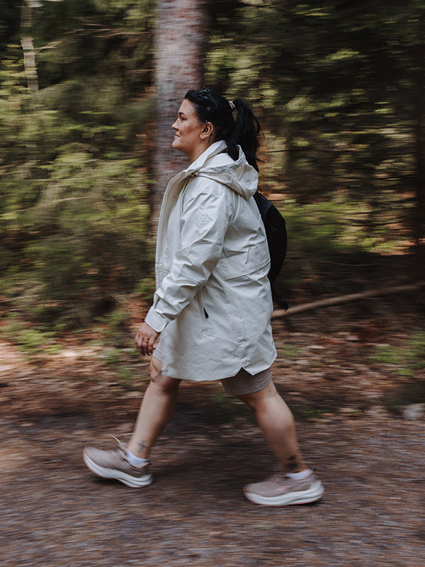 Wearing a Halti Kallas DX Parka Jacket Plus Womens and sneakers, a person walks along a tree-lined forest trail.