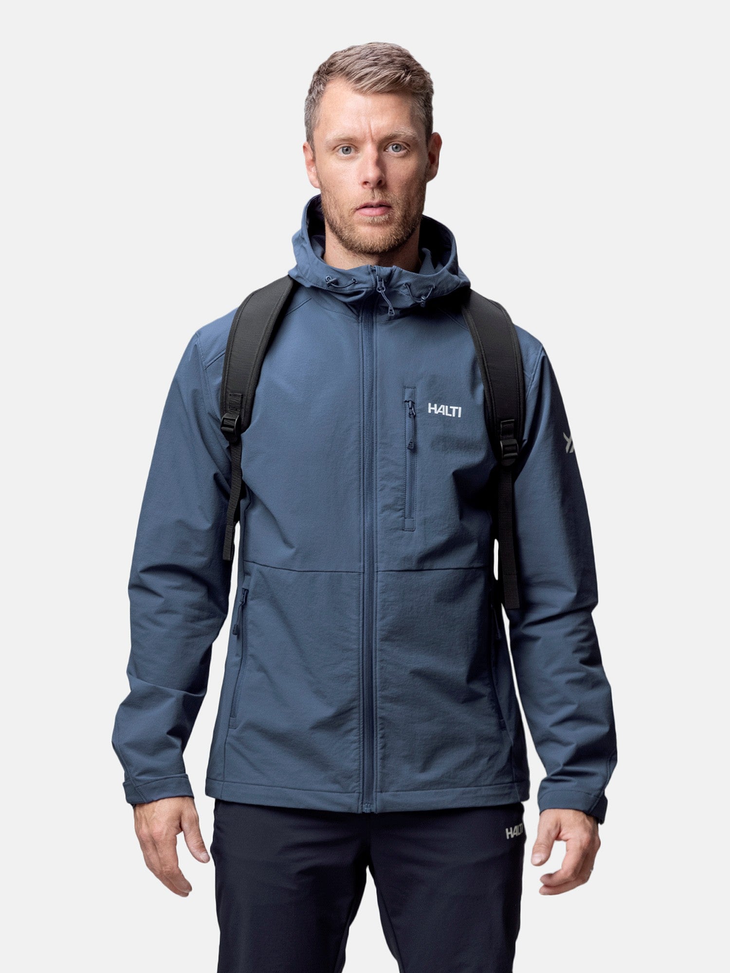A man wears the Halti Finholma X-stretch Jacket and a black backpack, standing against a plain background.