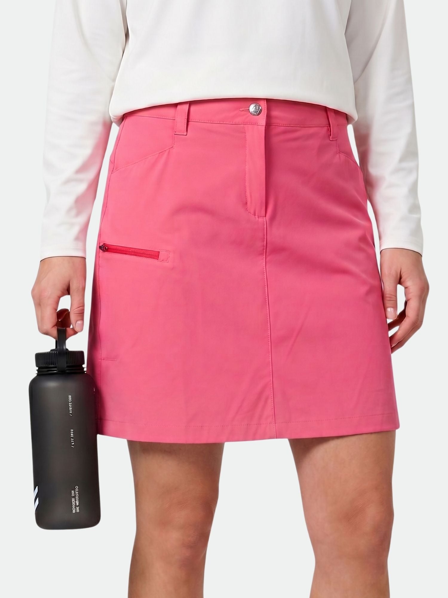 Wearing the Halti Pallas Cool Skort, a woman in pink holds a black water bottle by her side.