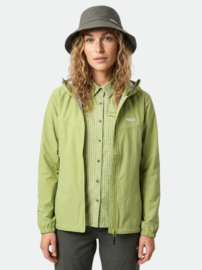 A woman wears the Halti Samoy Trekking Shirt Women's, a green jacket, and gray bucket hat against a white background.