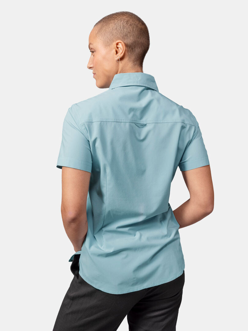 Woman with short hair wears Halti Samoy Trekking Shirt Women’s in light blue and dark pants, shown from the back.
