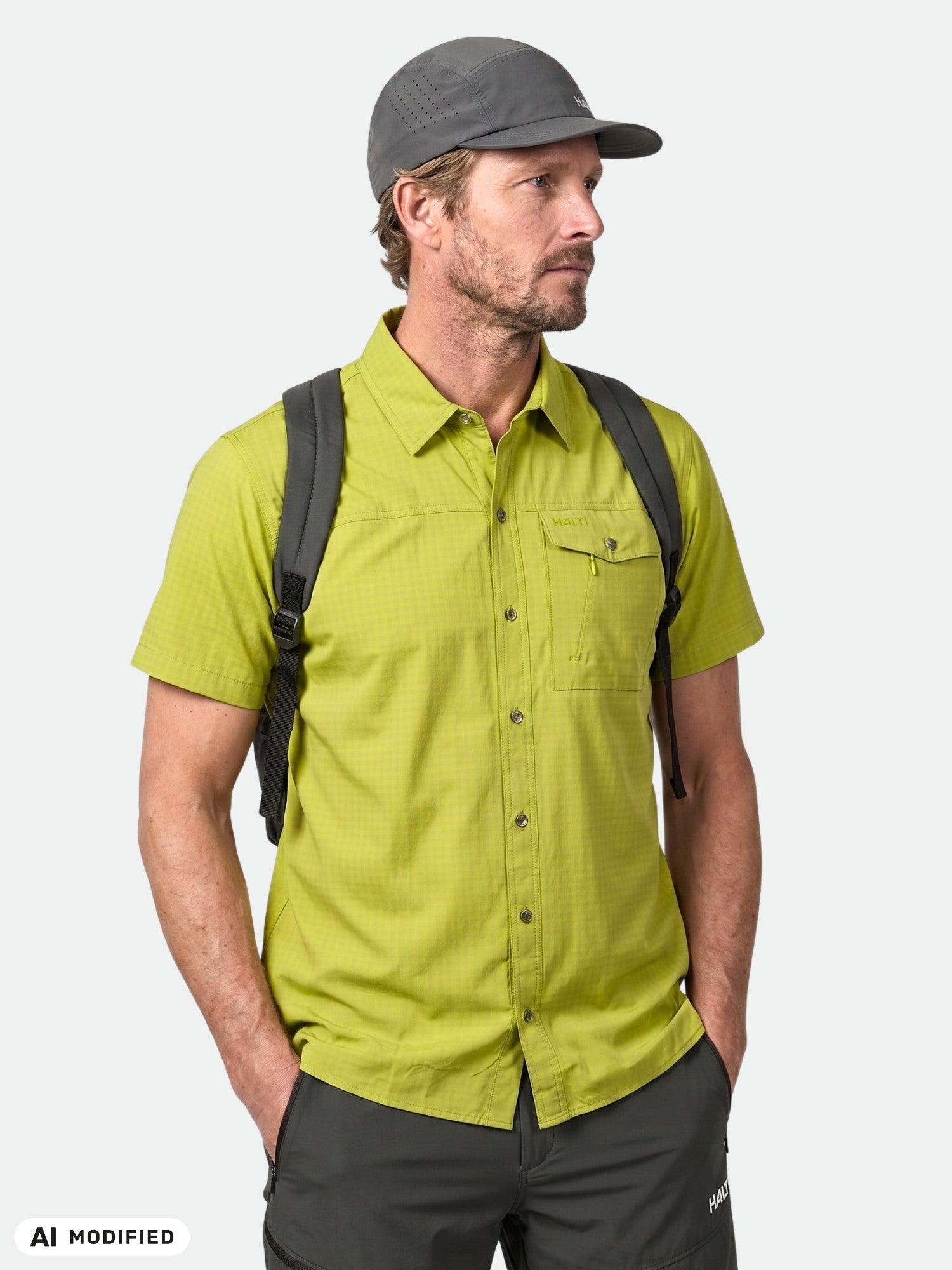 Man in Halti Samoy Trekking Shirt, gray cap, black backpack stands against a plain background.