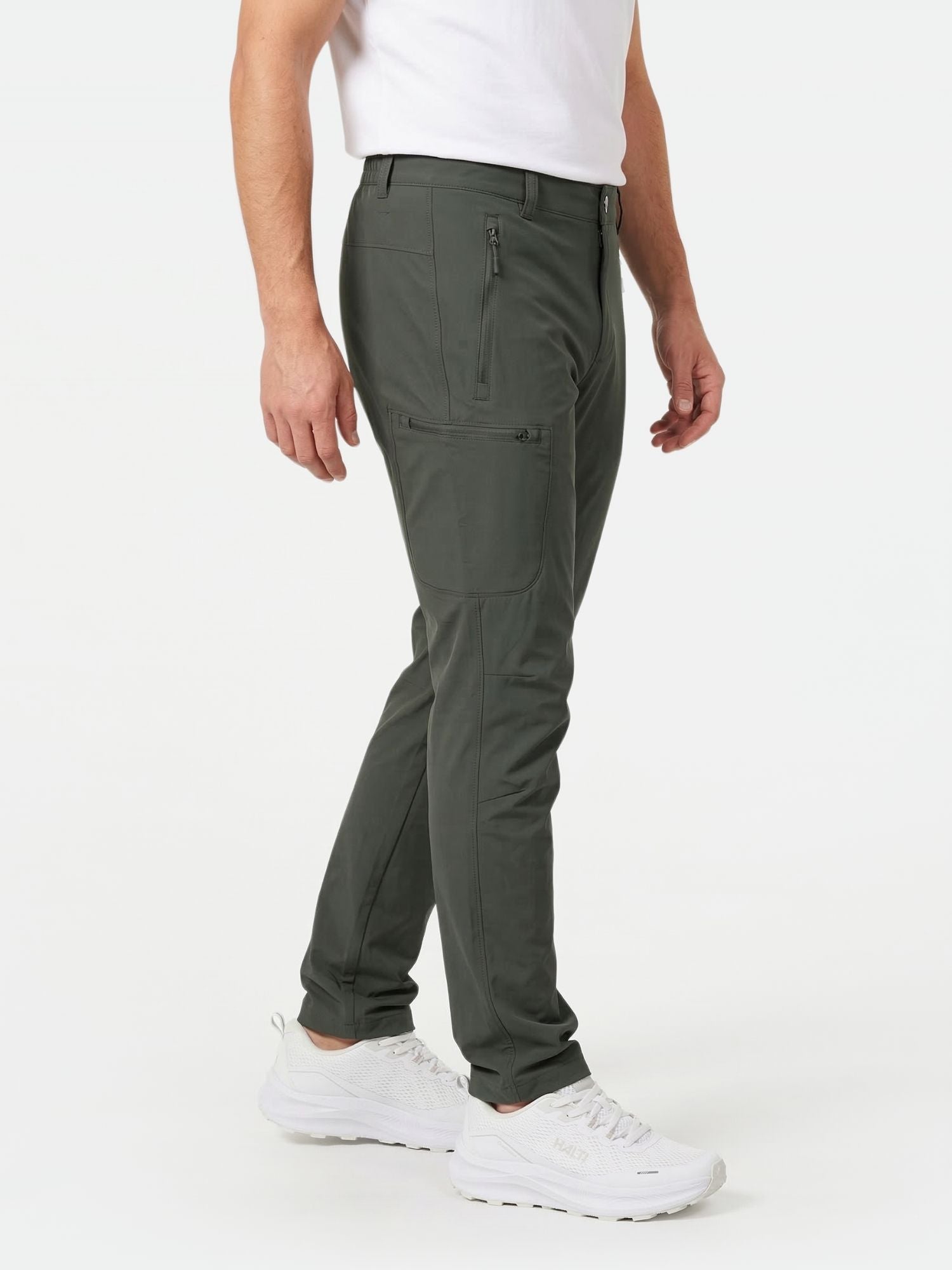 A person wears Halti Pallas X-stretch Outdoor Pants Men's in dark green, a white t-shirt, and white sneakers.