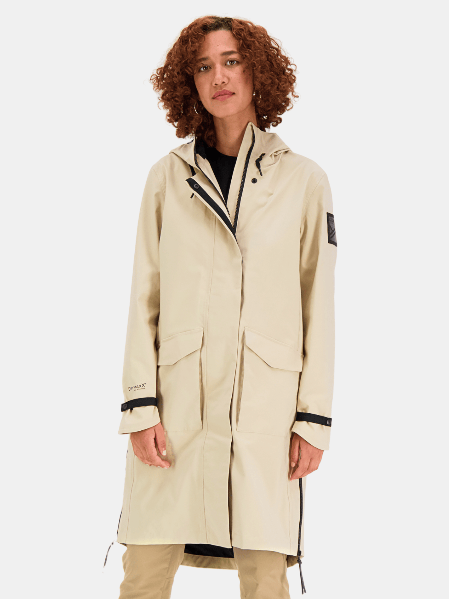 A person with curly hair wears the Halti Tokoi Womens DrymaxX Parka Jacket in beige, standing against a plain background.