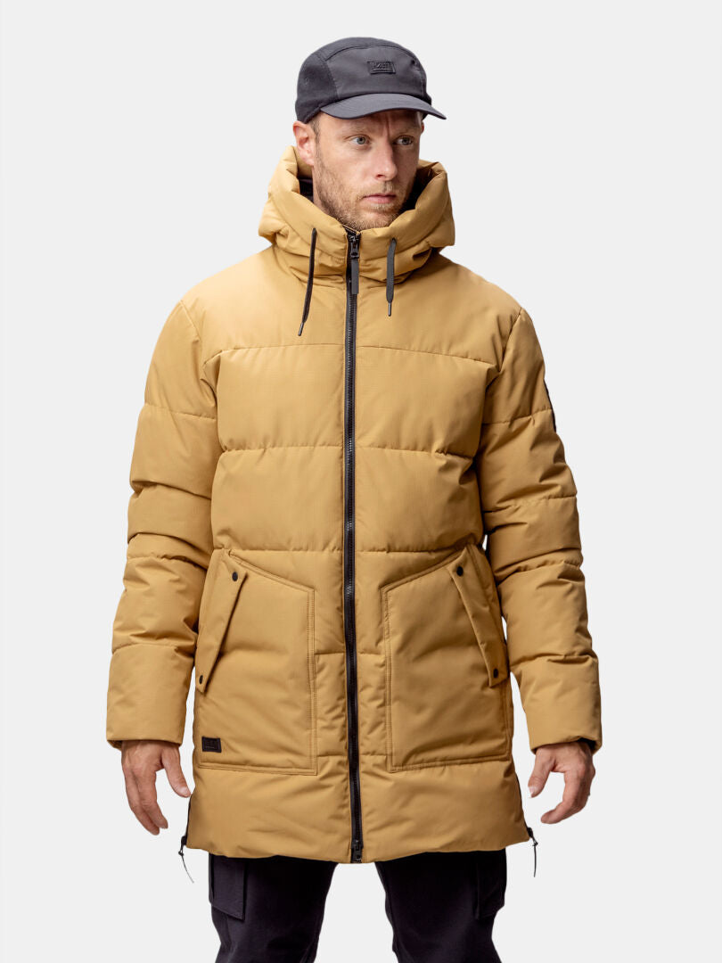 Man wearing the Halti Linjat Parka Jacket Men's in tan with hood and black zipper, plus a black cap and pants, facing forward.