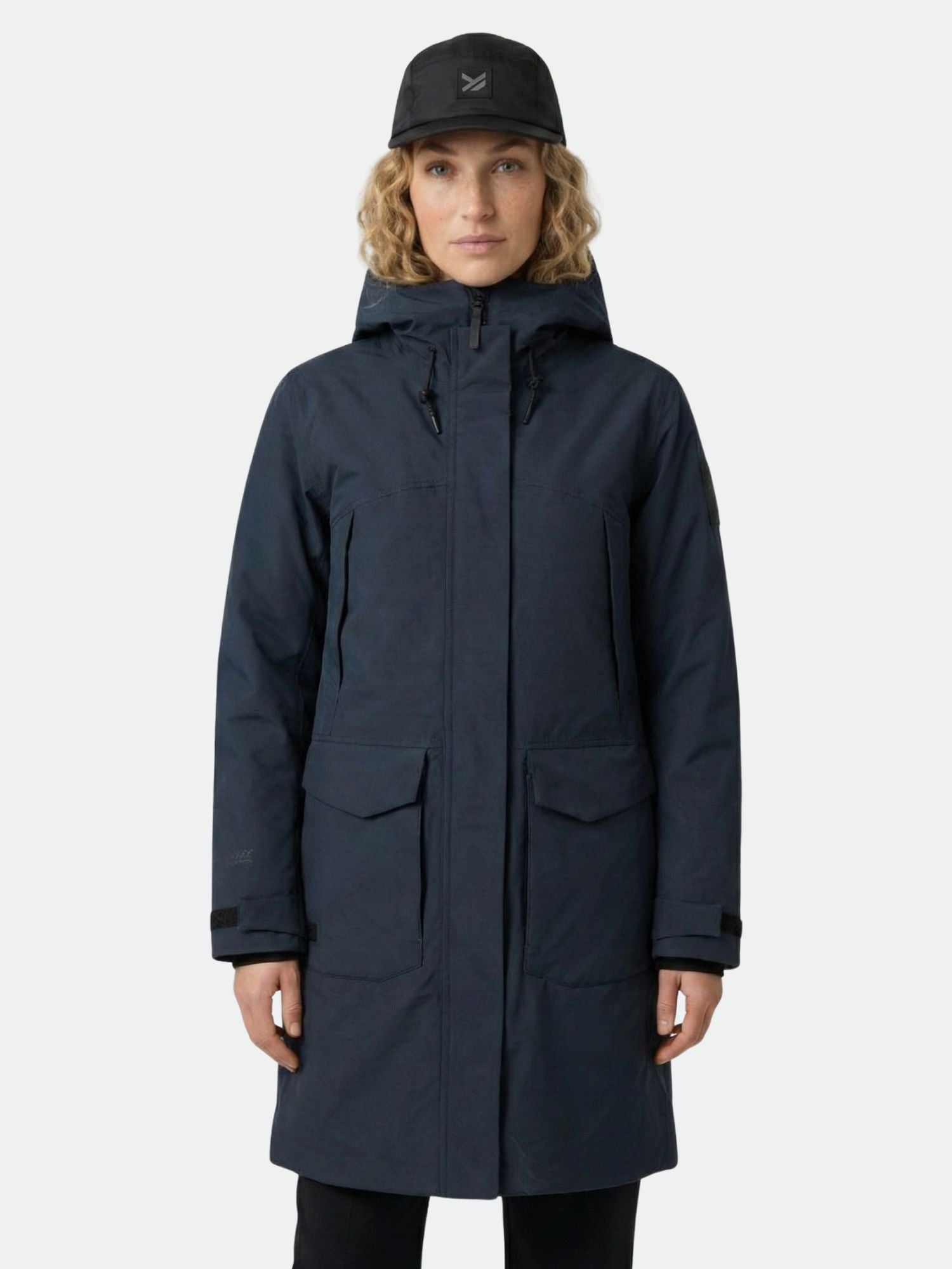 Model wears the Halti Bergga Women's DrymaxX Winter Parka in dark blue and a black cap, against a light gray background.
