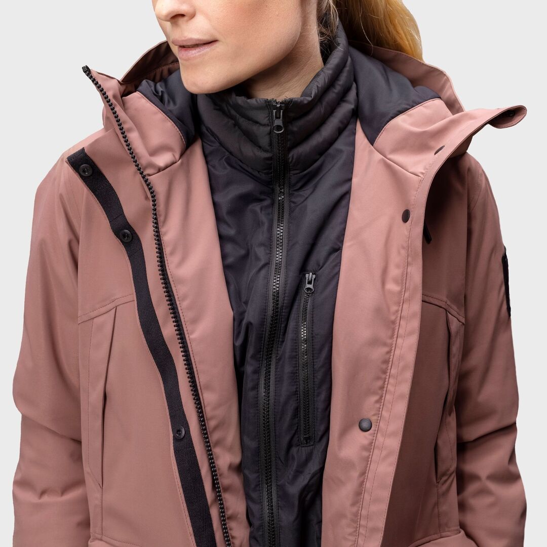 A woman wears a mauve Halti Bergga Womens DrymaxX Winter Parka over a black zip-up puffer vest.
