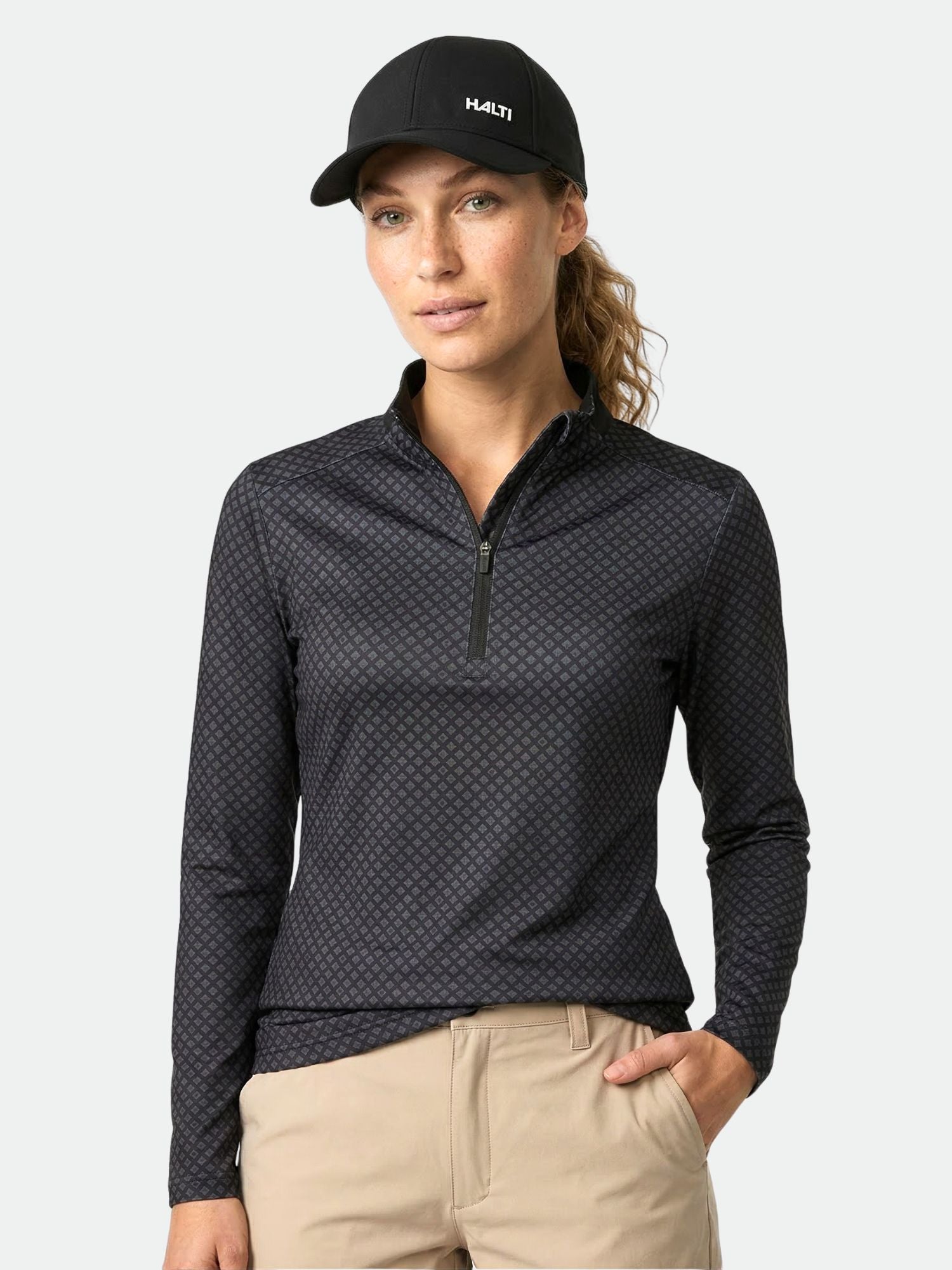 Woman in a Halti Fairway Women's Long Sleeve Shirt, beige pants, and black cap stands against a plain background.