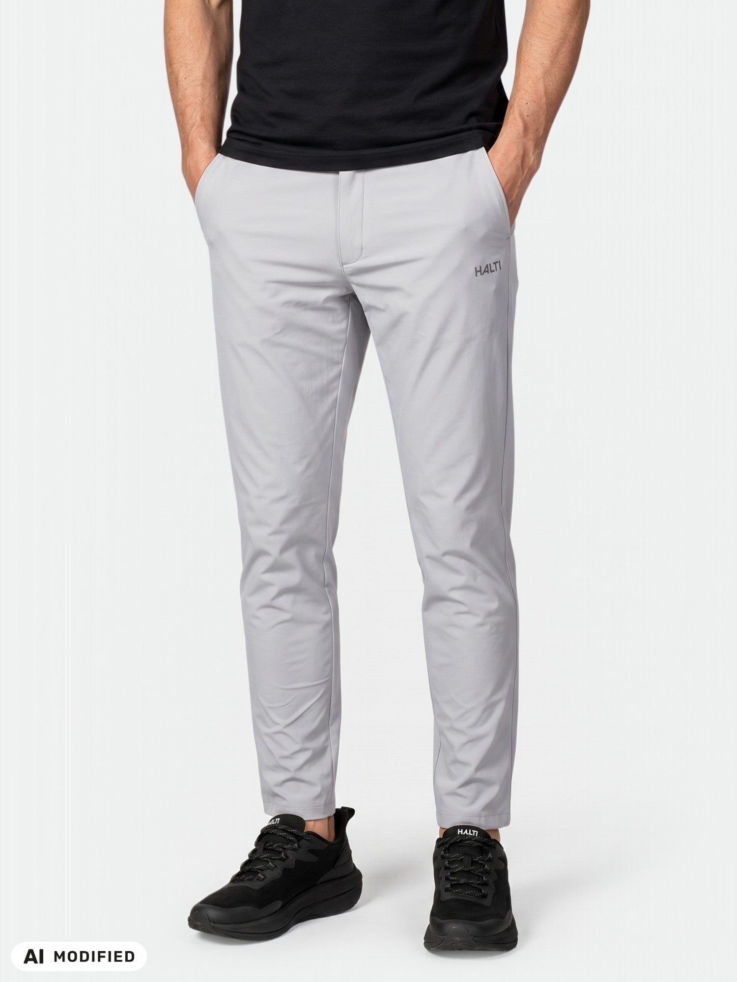 Person wearing Halti Drive X-stretch Chinos in light gray, black shirt, and sneakers, standing hands in pockets.