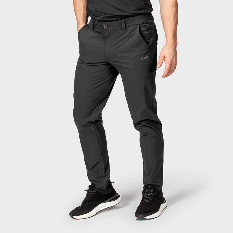 A person wears Halti Drive X-stretch Chinos, a black belt, and sneakers, hands in pockets against a plain background.
