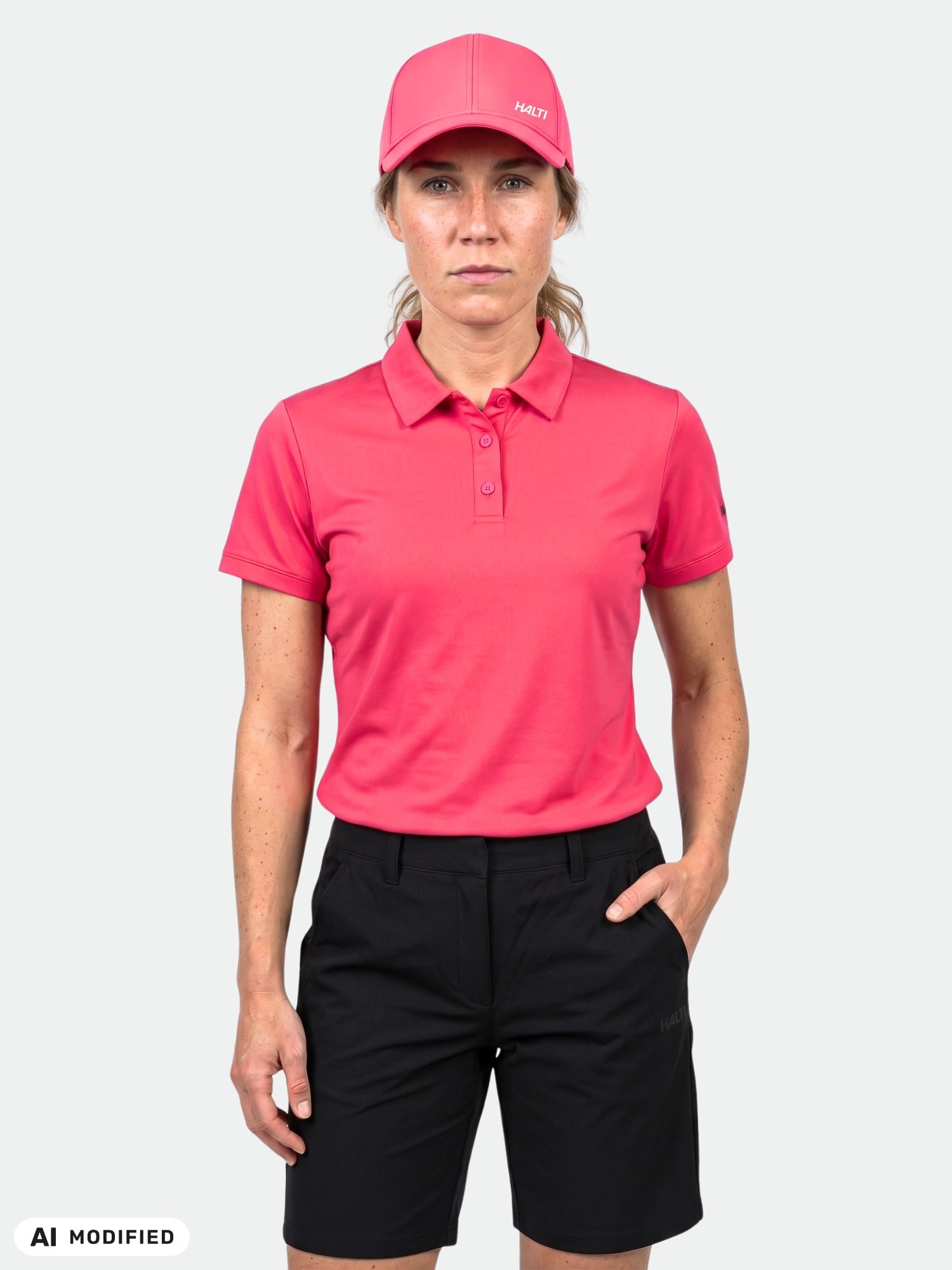 Model wears Halti Laine Technical Polo Shirt (women's), pink cap, and black shorts against a plain white background.