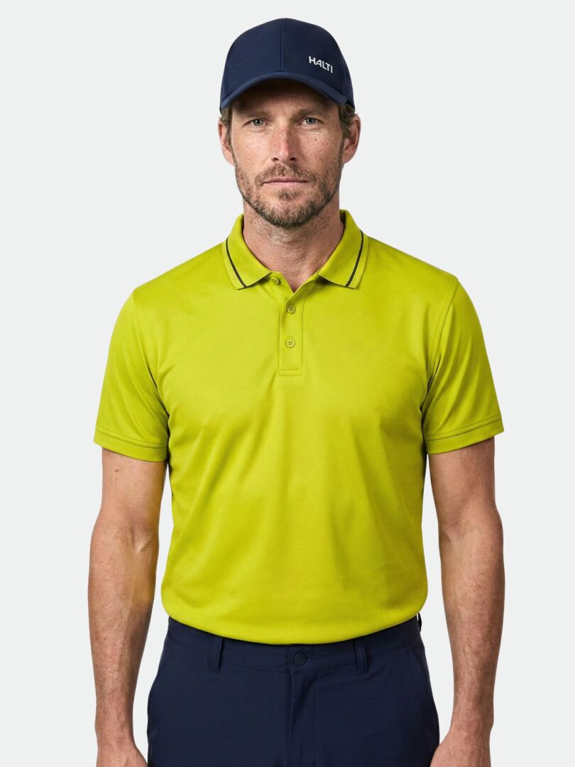 A man wears a Halti Laine Technical Polo Shirt in lime green and a navy cap, standing against a plain light background.