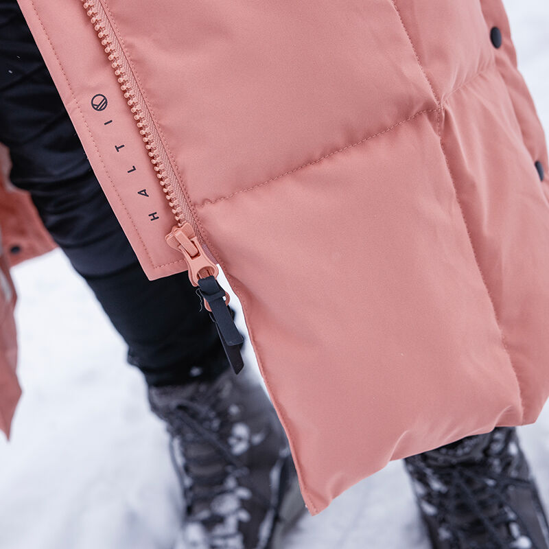 Close-up of Halti Penger Winter Jacket Womens zipper, black pants, and snow boots on snowy ground.