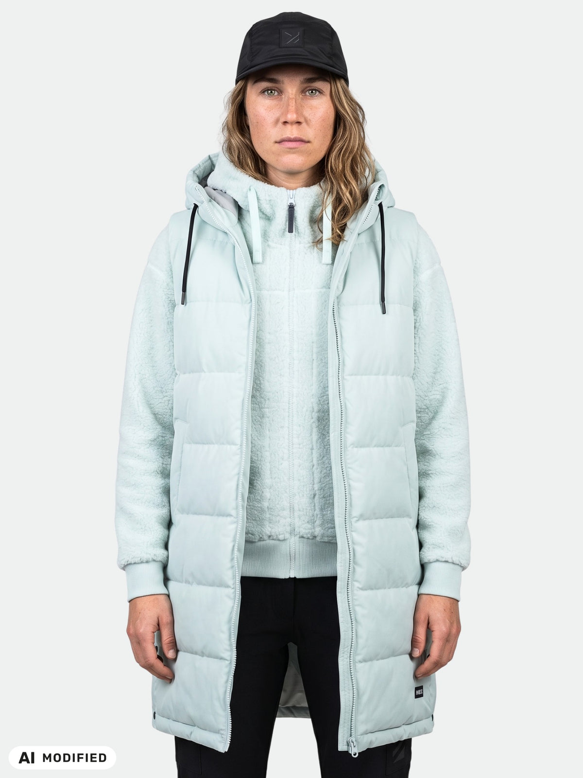 Woman in Halti Penger Puffer Vest (light blue), zip hoodie, black pants, and black cap, facing forward.