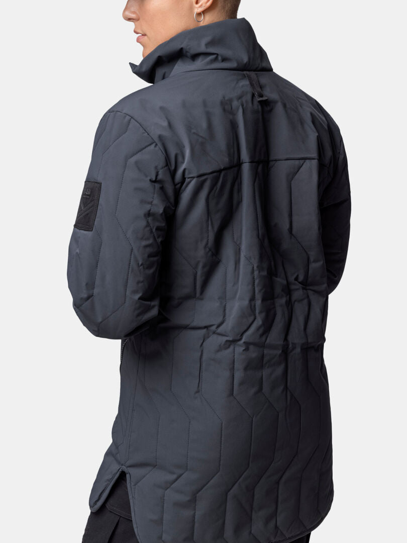 Woman wearing a Halti Synkas 3in1 DrymaxX Parka, long and dark with high collar and upper arm patch, viewed from behind.