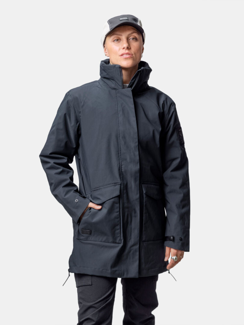 Person in Halti Synkas 3in1 DrymaxX Parka, black pants, and a light cap stands against a plain white background.