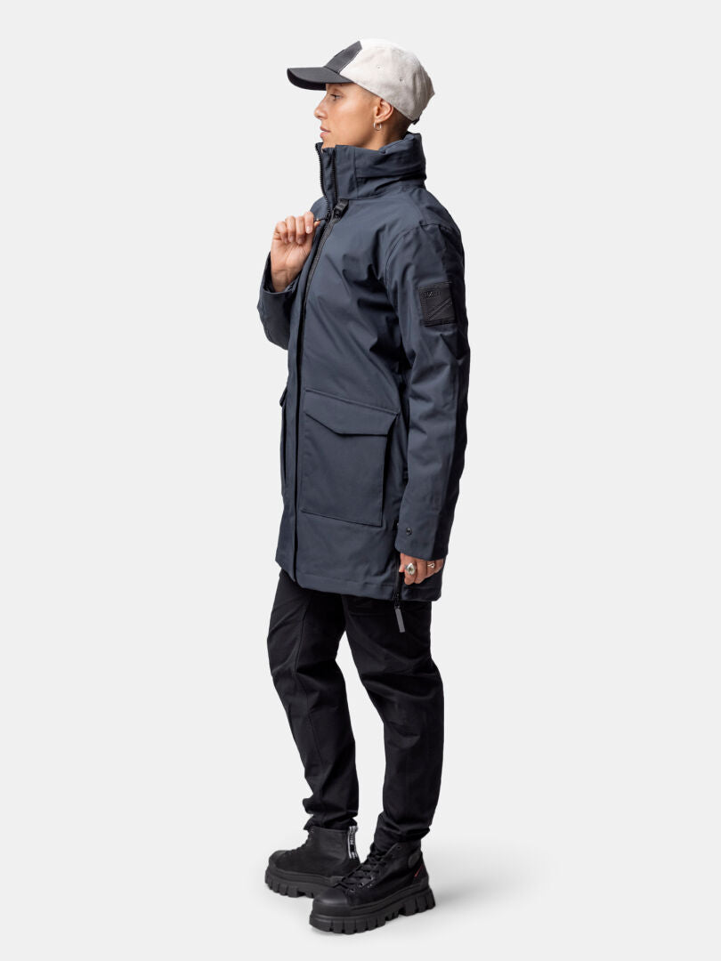 A woman wears the Halti Synkas 3in1 DrymaxX Parka and black pants, standing sideways against a plain background.