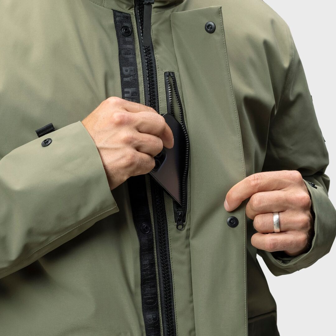 A person puts a smartphone into the zippered chest pocket of the Halti Synkas 3in1 DrymaxX Parka Mens.