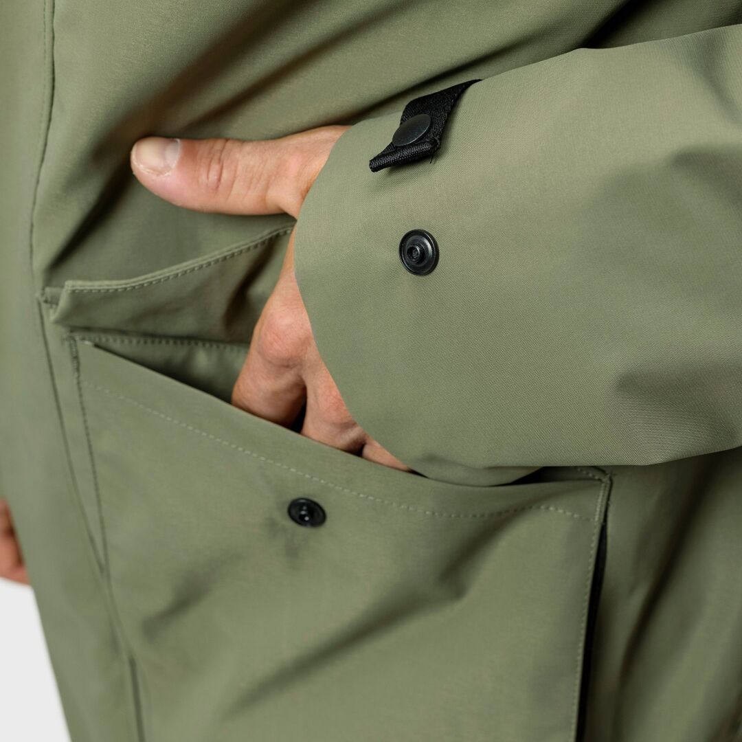 A hand reaches into the front pocket of the Halti Synkas 3in1 DrymaxX Parka Mens, featuring black snap buttons.
