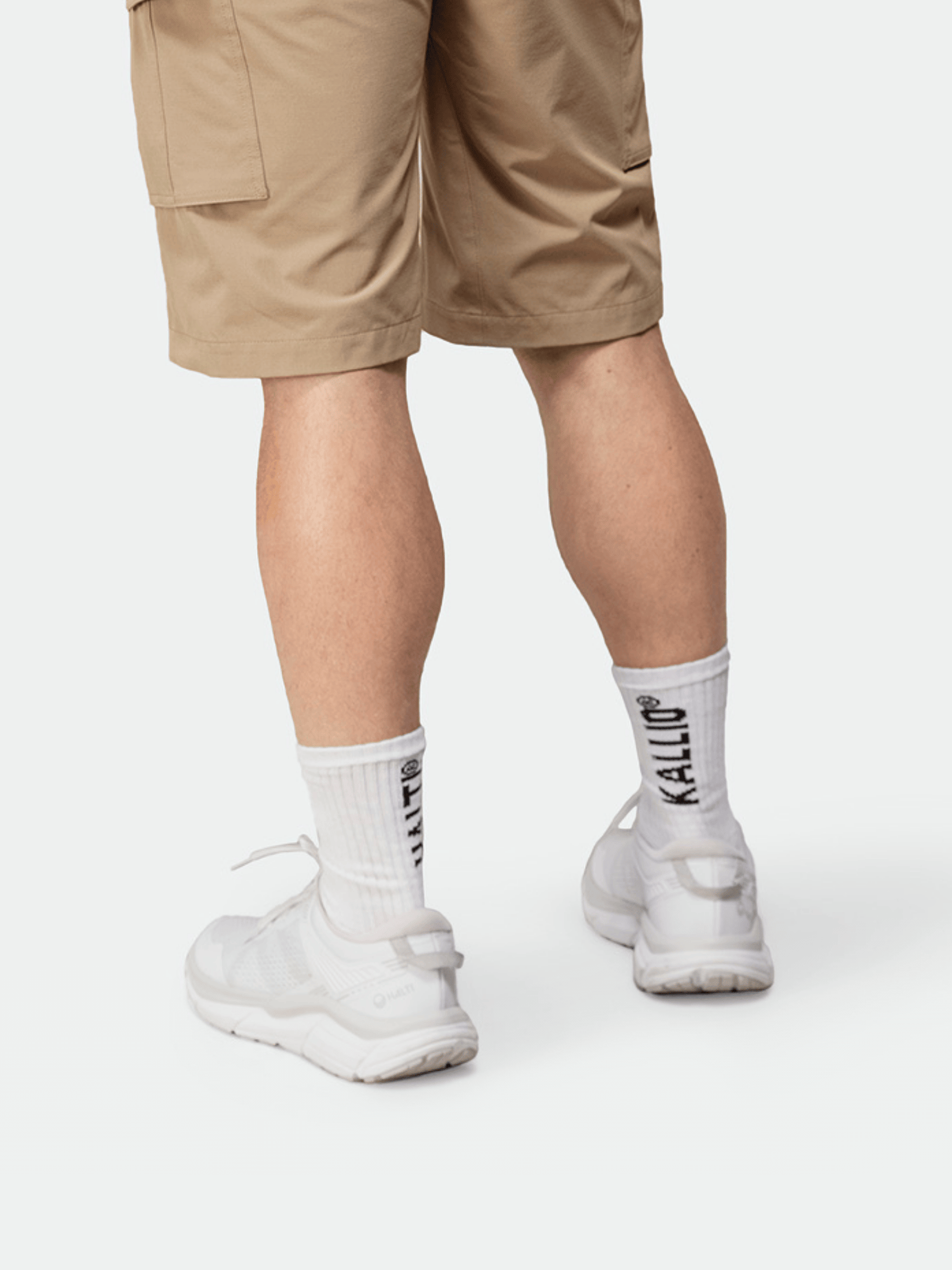 Person in tan shorts, white sneakers, and black Halti Kallio socks, highlighting sporty fashion.