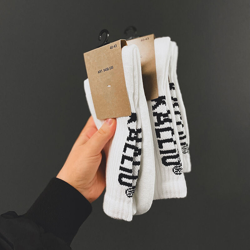 A hand holds two pairs of Halti Kallio white crew socks with black text, each packed with a brown card tag. Sports style.
