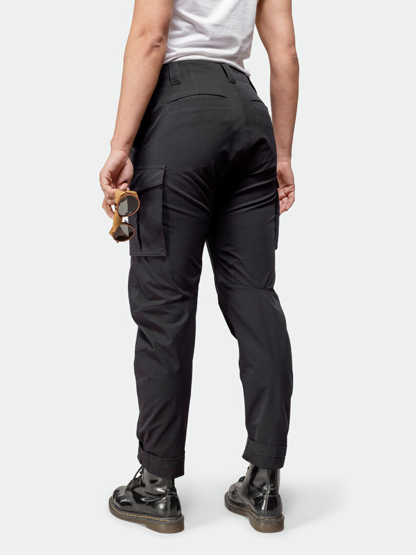 Person wearing Halti Roams Cargo Pants Womens, white shirt, black boots, holding sunglasses with back to camera.