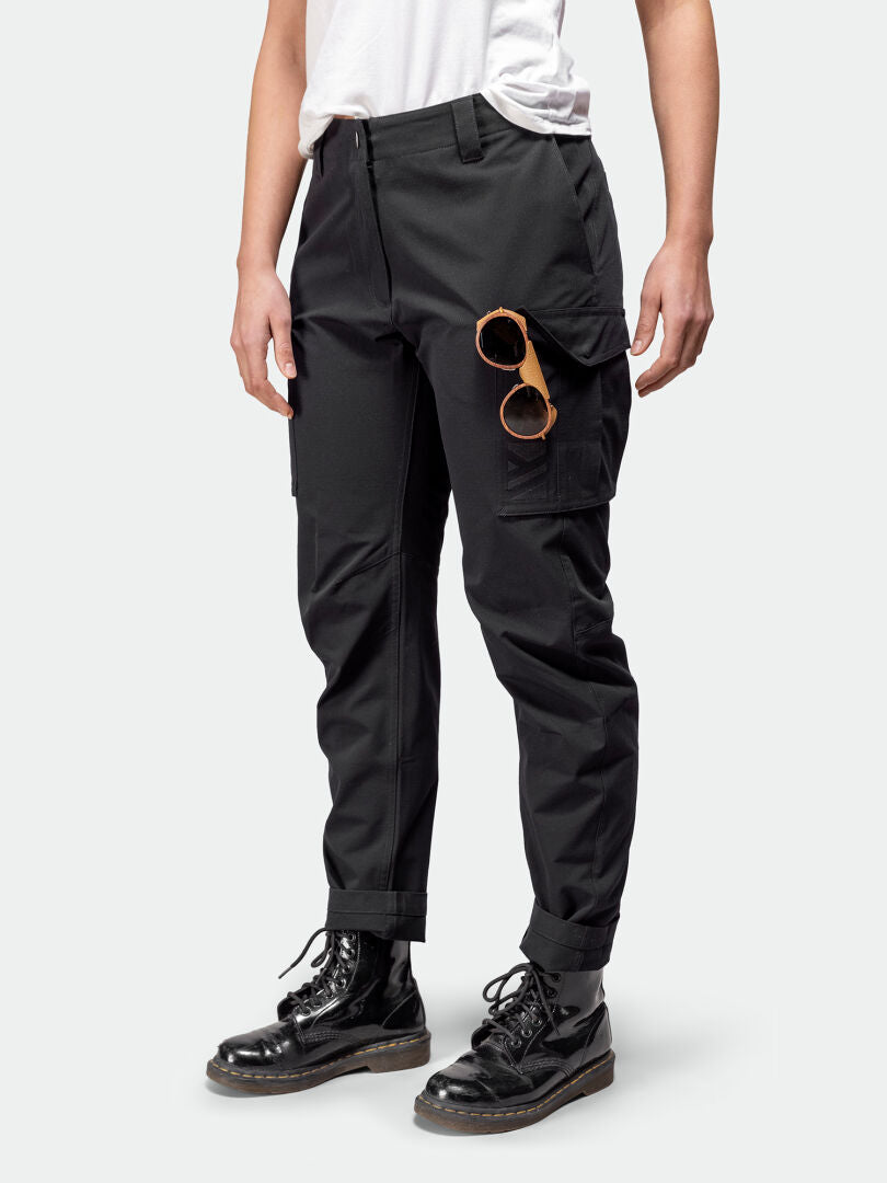 Model in Halti Roams Cargo Pants Womens, white tee, black boots, with sunglasses clipped to a pocket on plain background.
